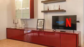 A modern living room with a red entertainment unit, a flat-screen TV displaying the Netflix logo, and a fireplace with decorative items.
