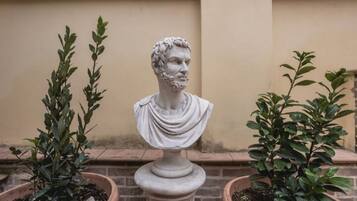 Une sculpture en marbre représentant un buste, placée entre deux plantes en pot.