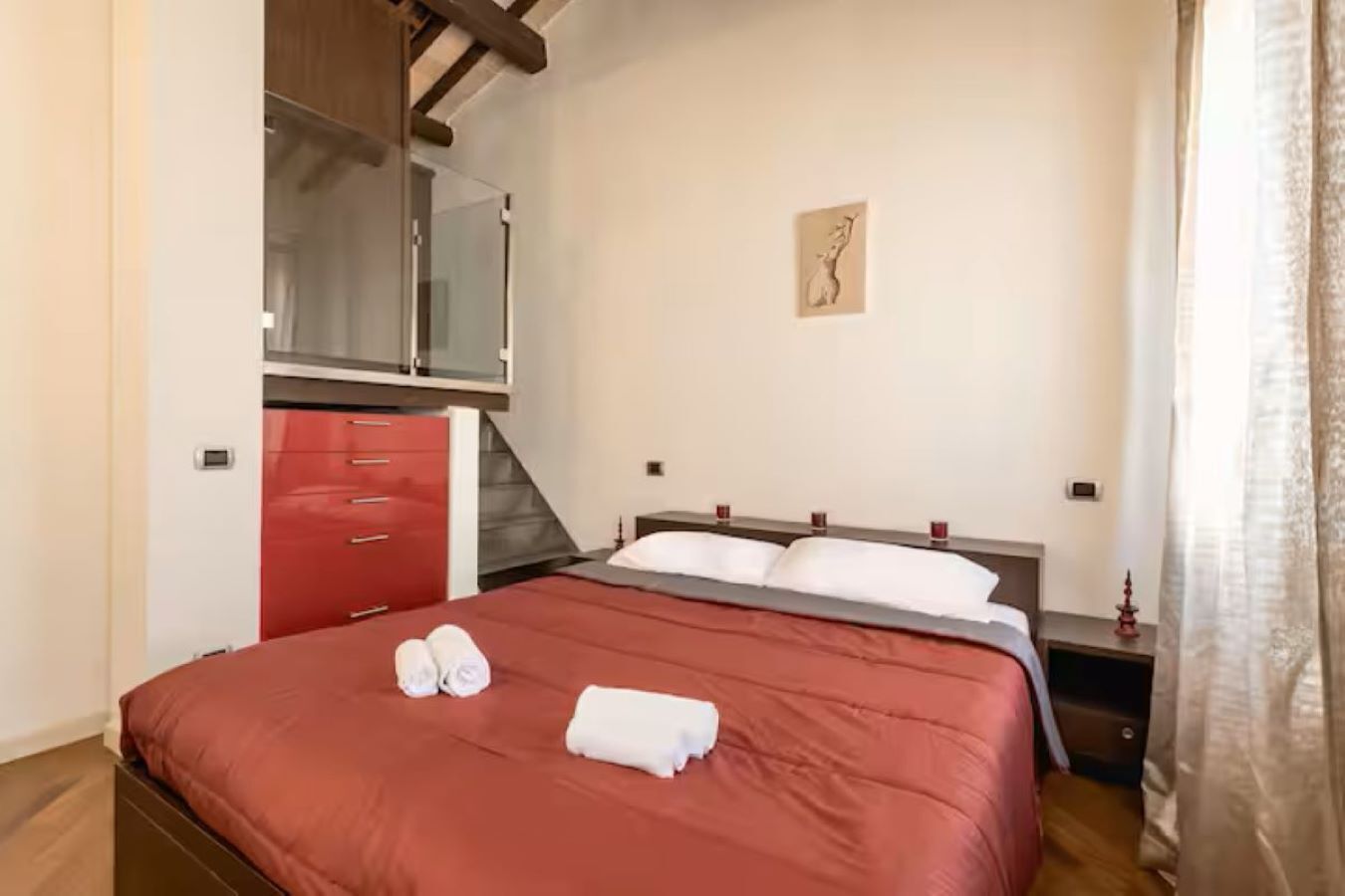 Ein Schlafzimmer mit einem Bett, einem roten Kleiderschrank, einem kleinen Nachttisch und einem an der Wand befestigten Kunstwerk.