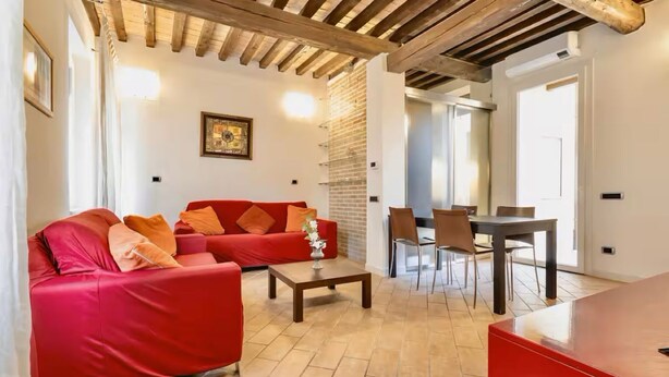 Ein Wohnzimmer mit rotem Sofa, einem Couchtisch und einem Essbereich mit Stühlen und Tisch.