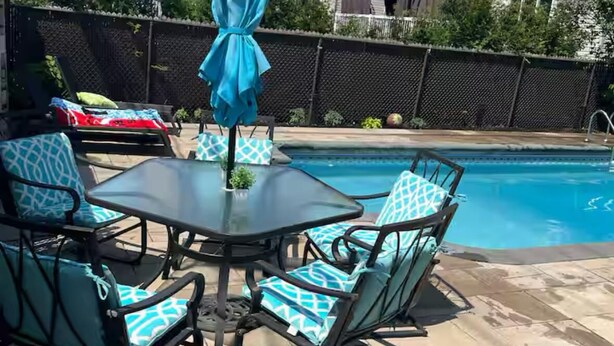 An outdoor patio with a pool table, chairs, and a blue umbrella.