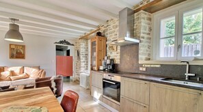Une cuisine chaleureuse avec des murs en pierre, des armoires en bois et une grande fenêtre.