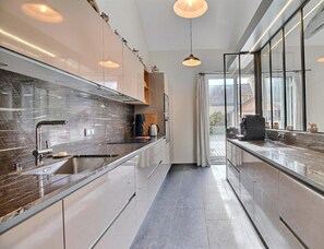 A modern kitchen with a sleek design, featuring a stainless steel sink, a marble countertop, and pendant lighting.
