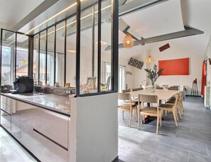 A modern kitchen with a large island, a dining area with a long table, and a living space with a fireplace. - Les Pommiers - GUIDEL (GUIDEL)