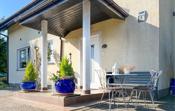 A building with a covered porch, two large potted plants, and a metal table with chairs.