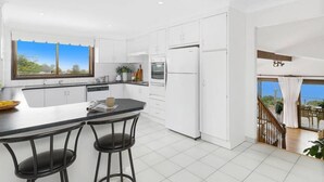 A modern kitchen with white cabinets, a black countertop, and two bar stools. - Entire spectacular lake and ocean view holiday house (Lake Heights)