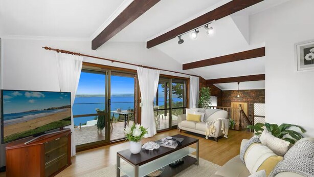 A spacious living room with a large TV, a coffee table, and a sofa. There is a balcony with a view of the sea. - Entire spectacular lake and ocean view holiday house (Lake Heights)