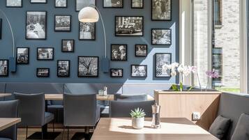 A modern dining area with a wall of black and white photographs, a wooden table, and grey upholstered seating.
