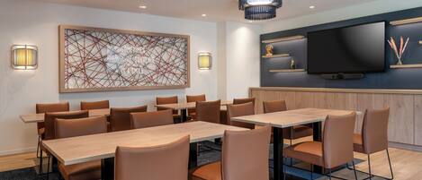 Un salón de conferencias de hotel con una mesa grande, varias sillas, un televisor de pantalla plana y decoración en la pared.