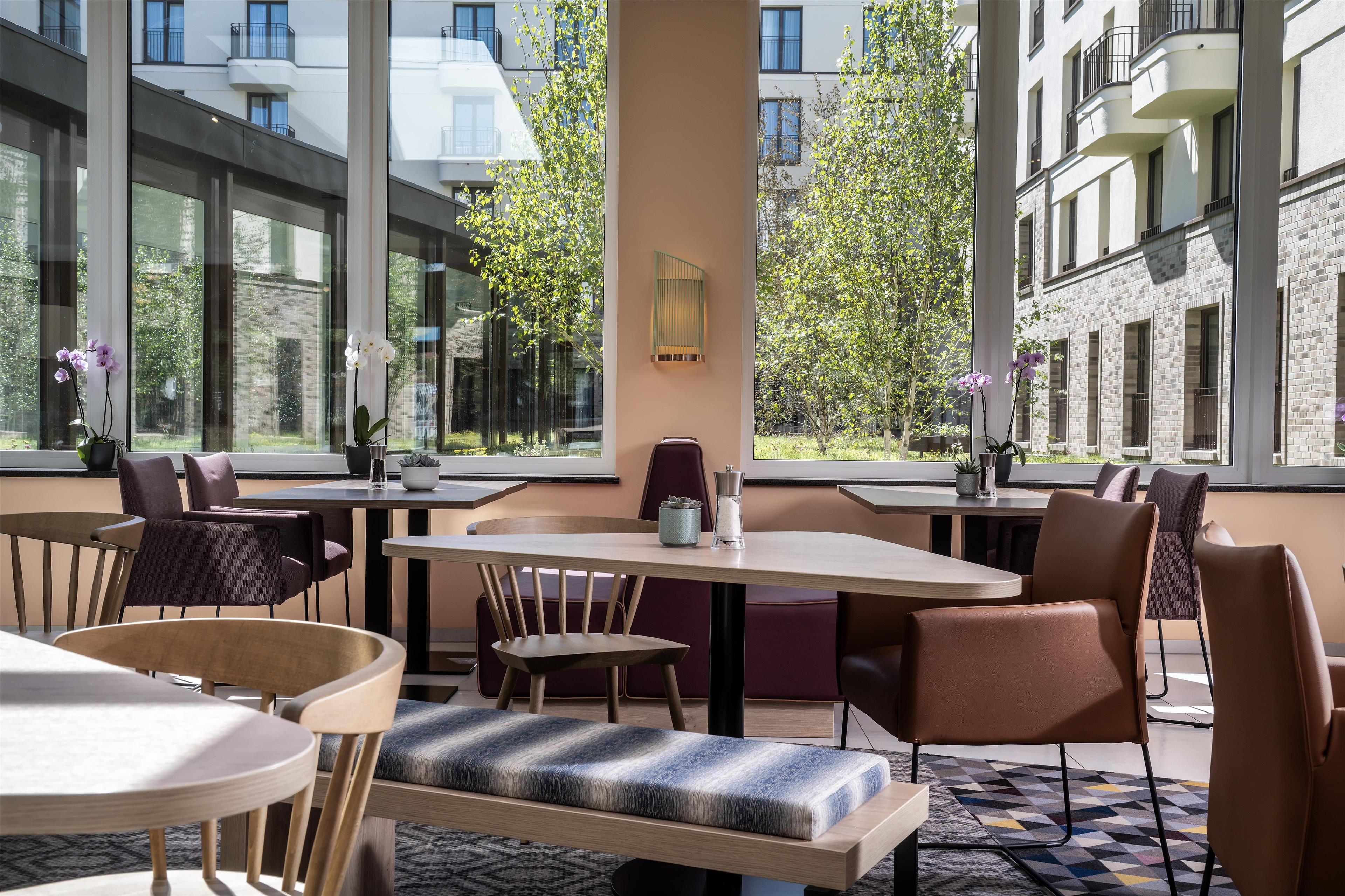 Un comedor moderno con mesas y sillas, ventanas amplias y vistas a edificios y árboles.