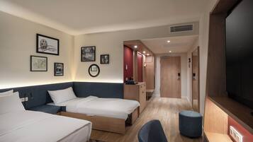 A hotel room with two beds, a desk, a chair, a TV, and artwork on the walls.
