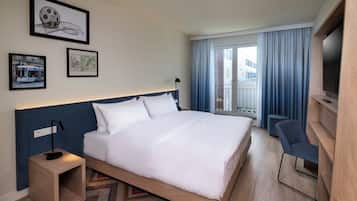 A modern hotel room with a large bed, a desk with a lamp, a TV, and framed pictures on the wall.