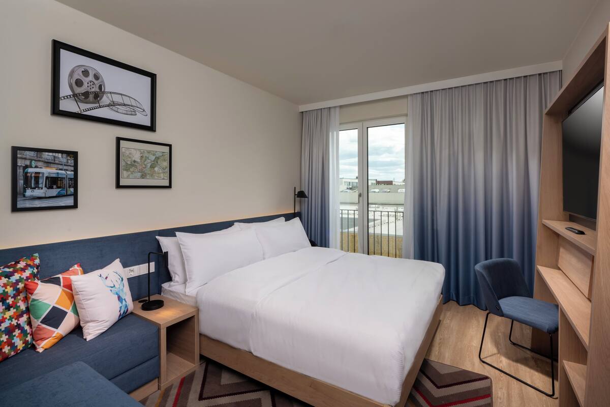 A hotel room with a large bed, a sofa, a TV, and a balcony with curtains.