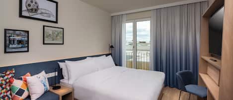 A hotel room with a large bed, a sofa, a TV, and a balcony with curtains.