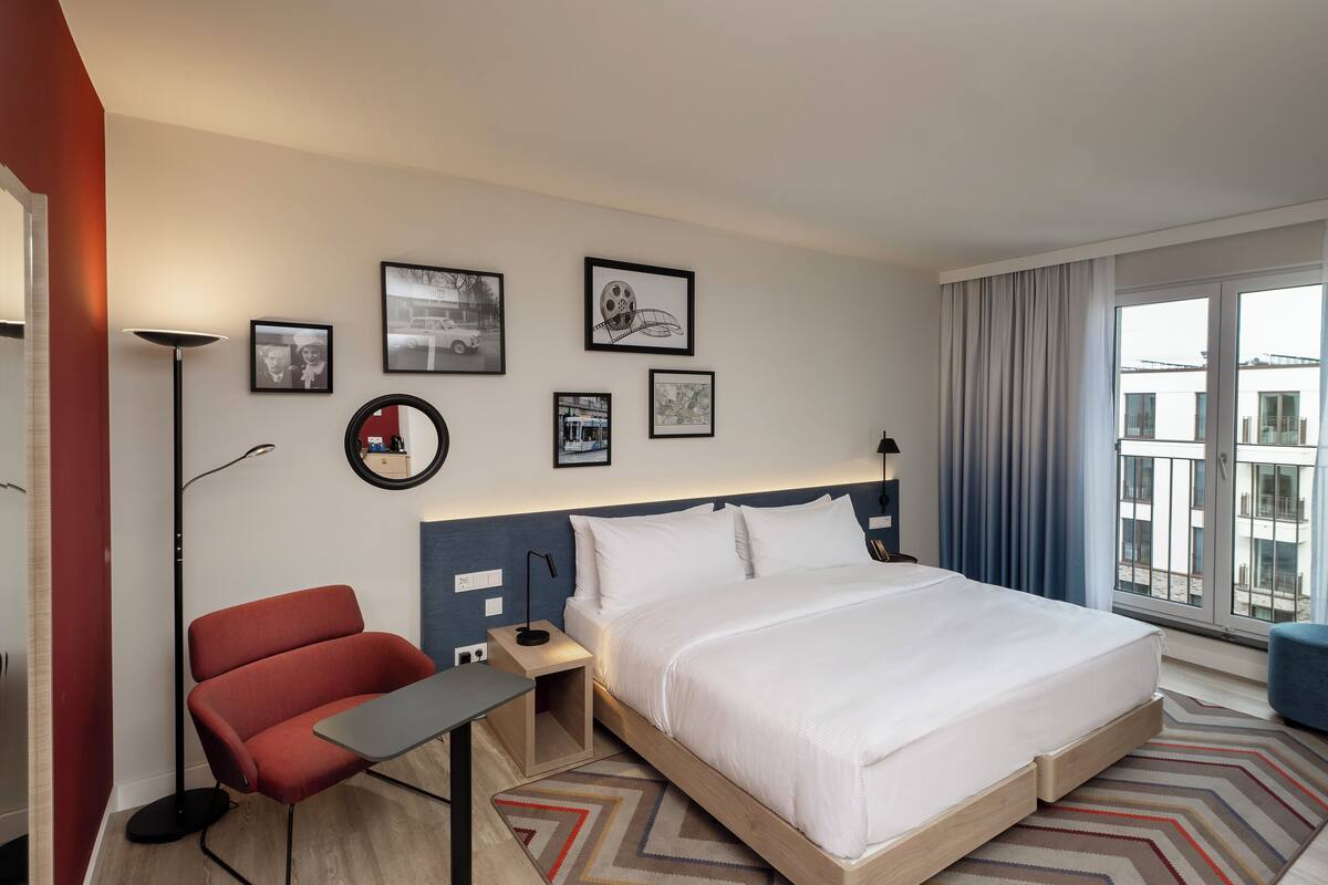A hotel room with a large bed, a desk, a chair, and a window with curtains.