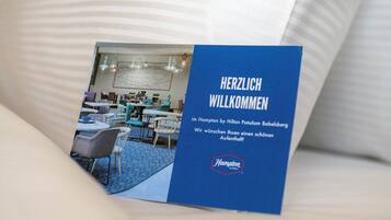 Eine Broschüre mit einem Foto einer Hotelhalle, die Tische, Stühle und Hängeleuchten zeigt.