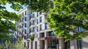 Un bâtiment moderne avec une enseigne indiquant « Hampton by Hilton ». Il est doté de nombreux balcons et de grandes fenêtres.