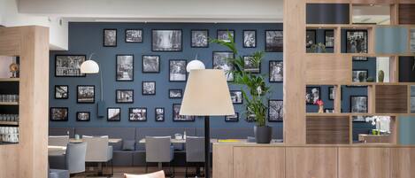 A modern interior with a round dining table, chairs, a lamp, and a wall adorned with black-and-white photographs.