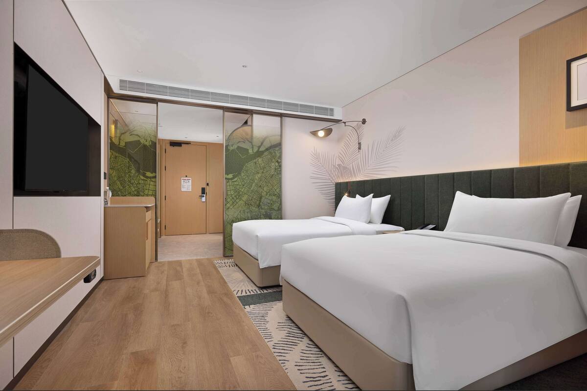 A hotel room with two beds, a desk, a TV, and a sliding door leading to a bathroom.
