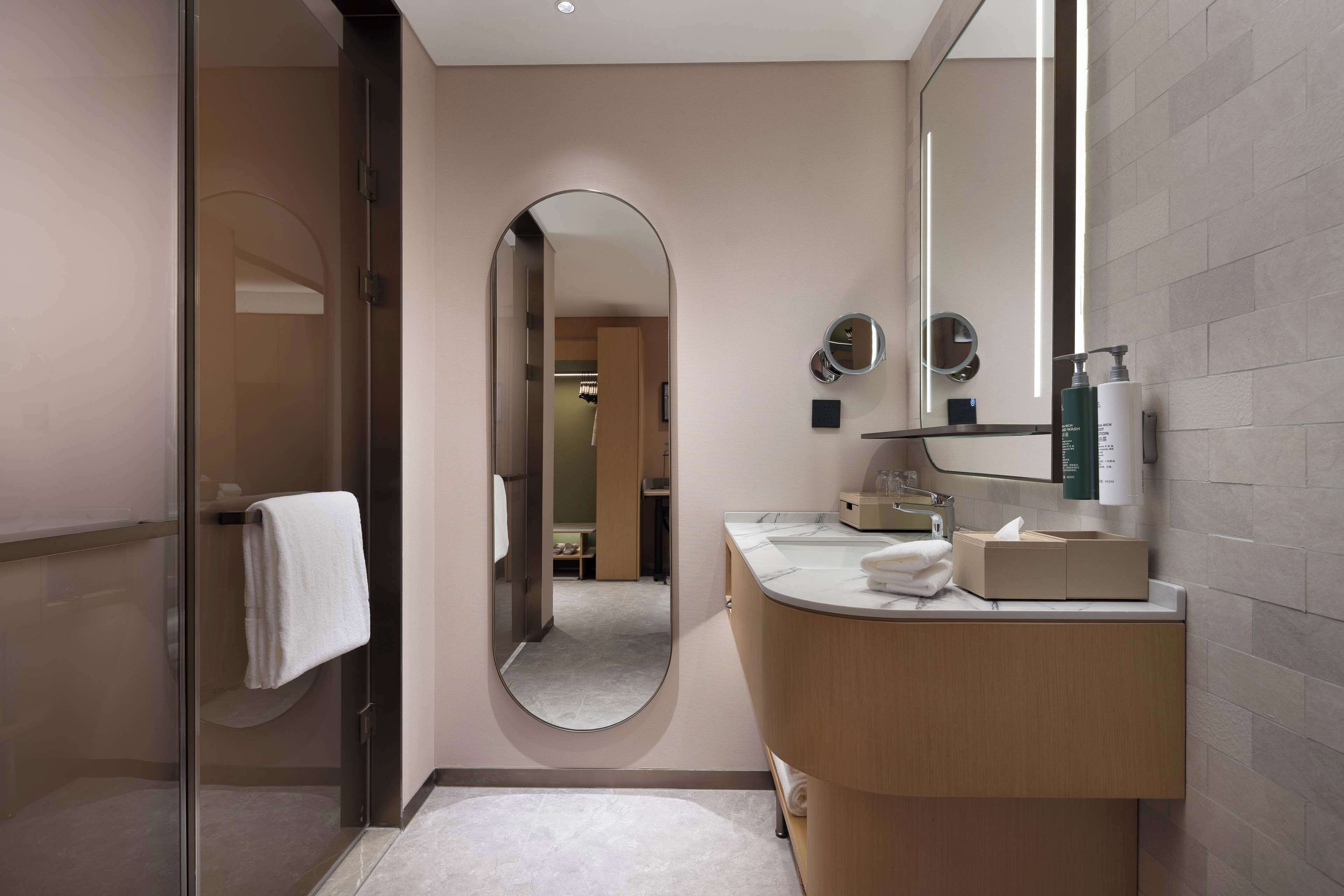 Une salle de bain moderne dotée d’une douche à parois de verre, d’un grand miroir et d’un meuble-lavabo en bois avec un évier et un porte-serviettes.