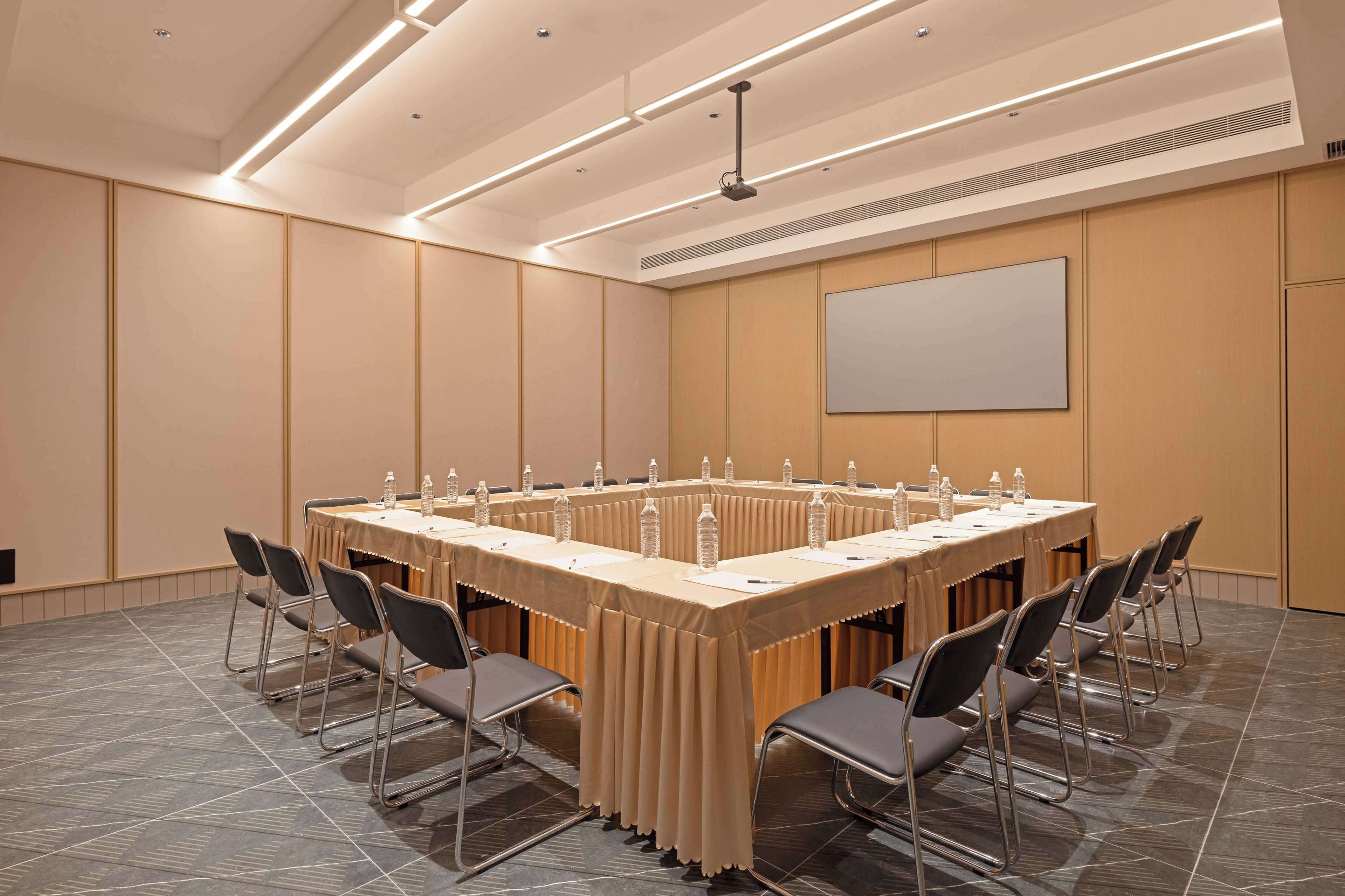 A conference room with a long table, chairs, and a projector screen.
