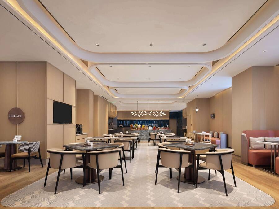 Un restaurante moderno con mesas y sillas redondas, una zona de bar y un área de estar con sofás.