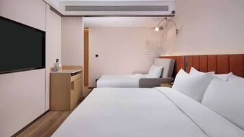 Habitación de hotel con una cama grande, una cama más pequeña, un escritorio con silla, un televisor y una lámpara de pared.
