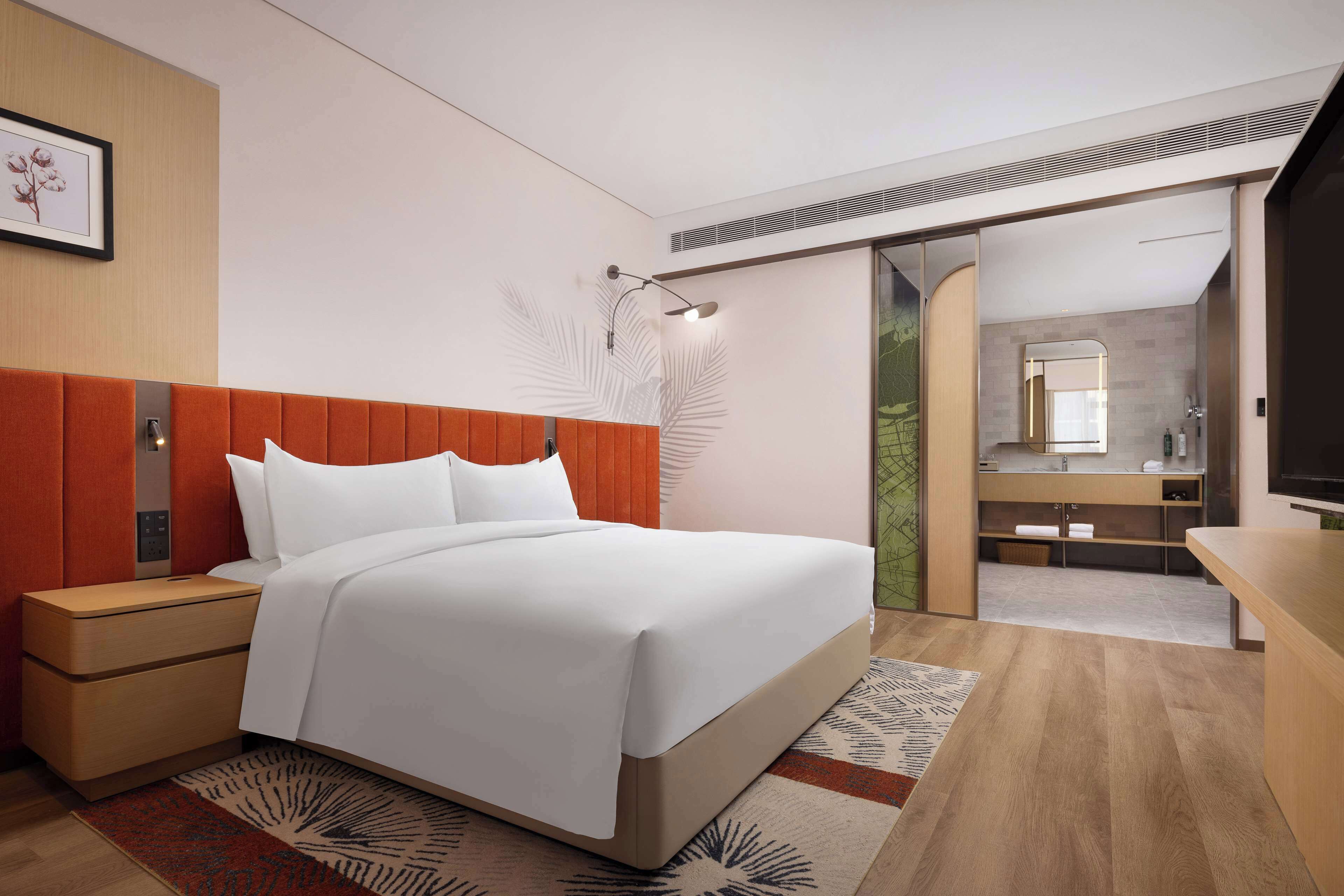 A modern hotel room with a bed, nightstand, and a bathroom visible through an open door.
