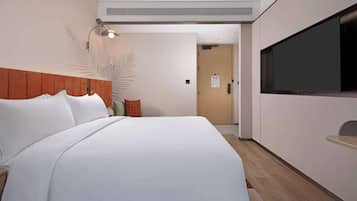 A hotel room with a large bed, a flat-screen TV mounted on the wall, a wooden headboard, and a wall-mounted lamp.