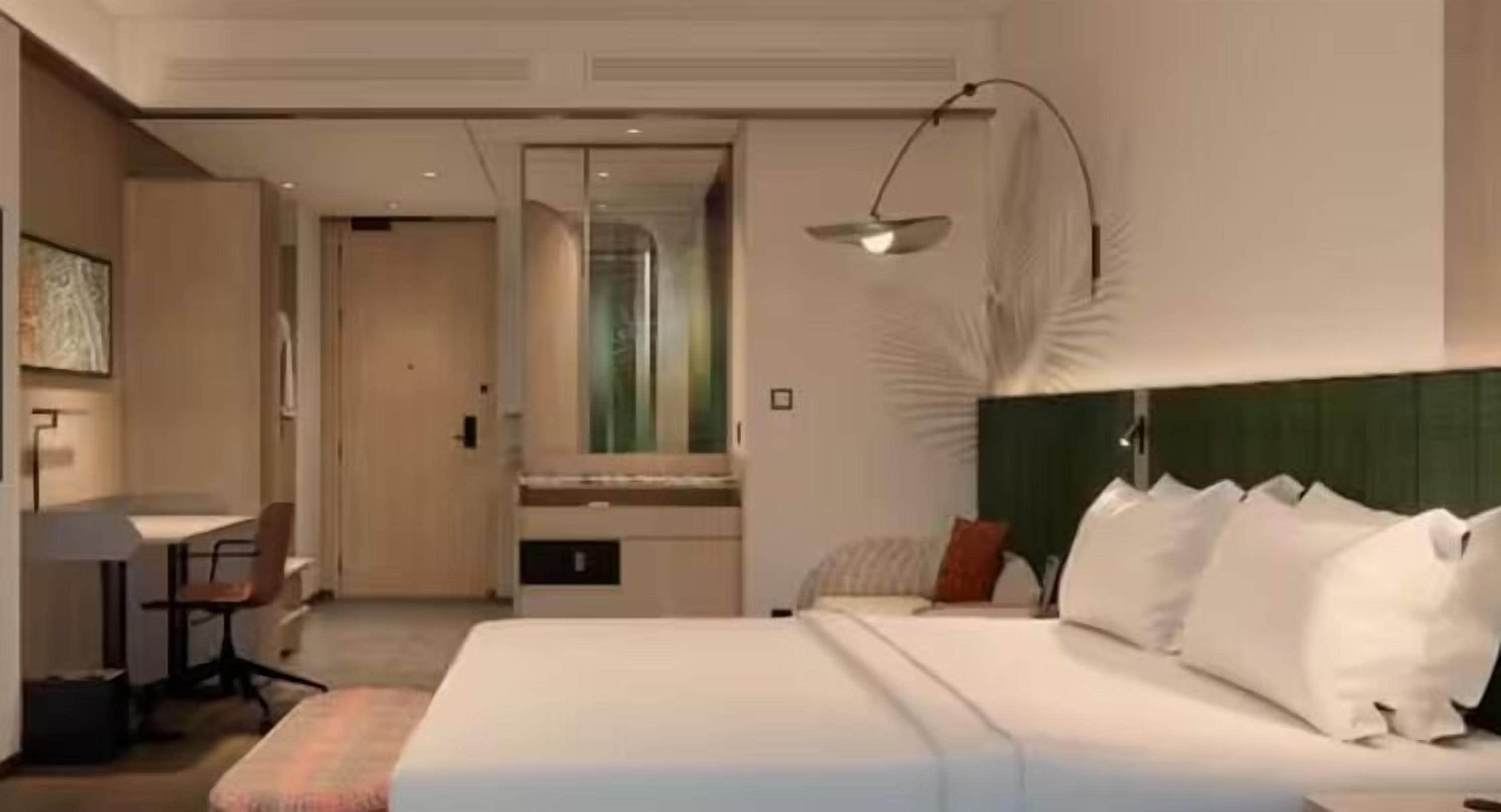 Une chambre d’hôtel avec un lit, une table de chevet, une lampe et une vue sur un couloir.