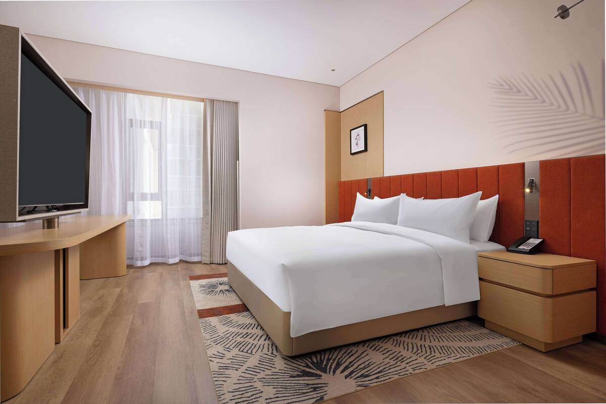 A hotel room with a bed, a TV, a desk, and a window with curtains.