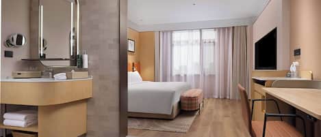 A hotel room with a bed, a desk, a chair, a vanity with a mirror, and a television.