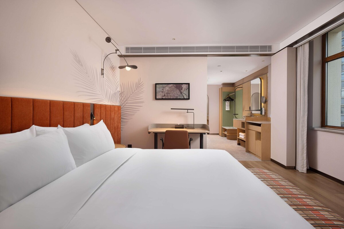 Una habitación de hotel con una cama grande, un escritorio con una silla, un espejo y una ventana.