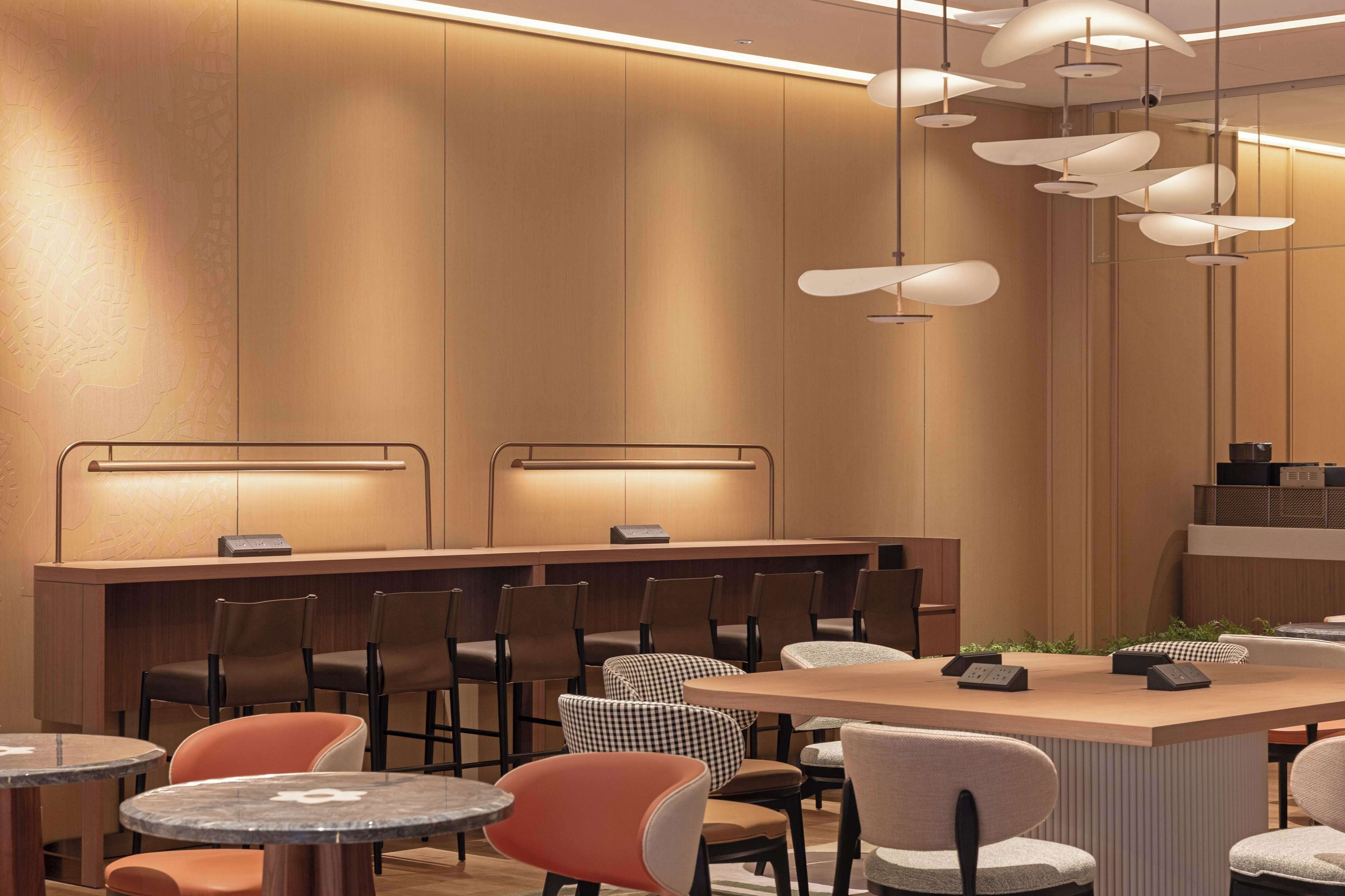A modern restaurant with a long counter, multiple chairs, and round tables.
