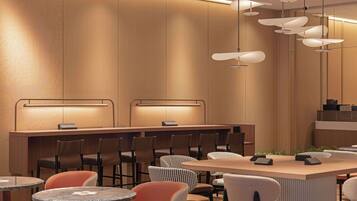 A modern restaurant with a long counter, multiple chairs, and round tables.