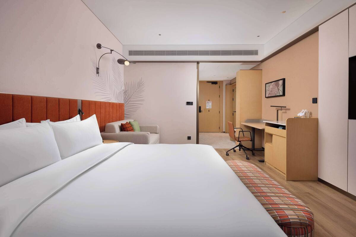 A modern hotel room with a large bed, a desk, and a seating area.