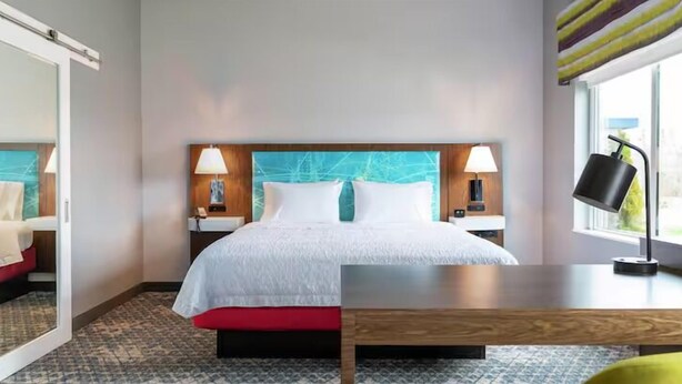 Een hotelkamer met een bed, nachtkastjes, lampen, een raam en een houten bureau.