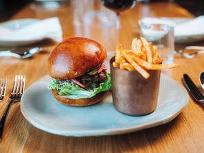 A plate with a burger and fries, a glass of red drink, and cutlery on a wooden table. - Skaneateles Fields Resort & Spa, Curio Collection By Hilton (Skaneateles)