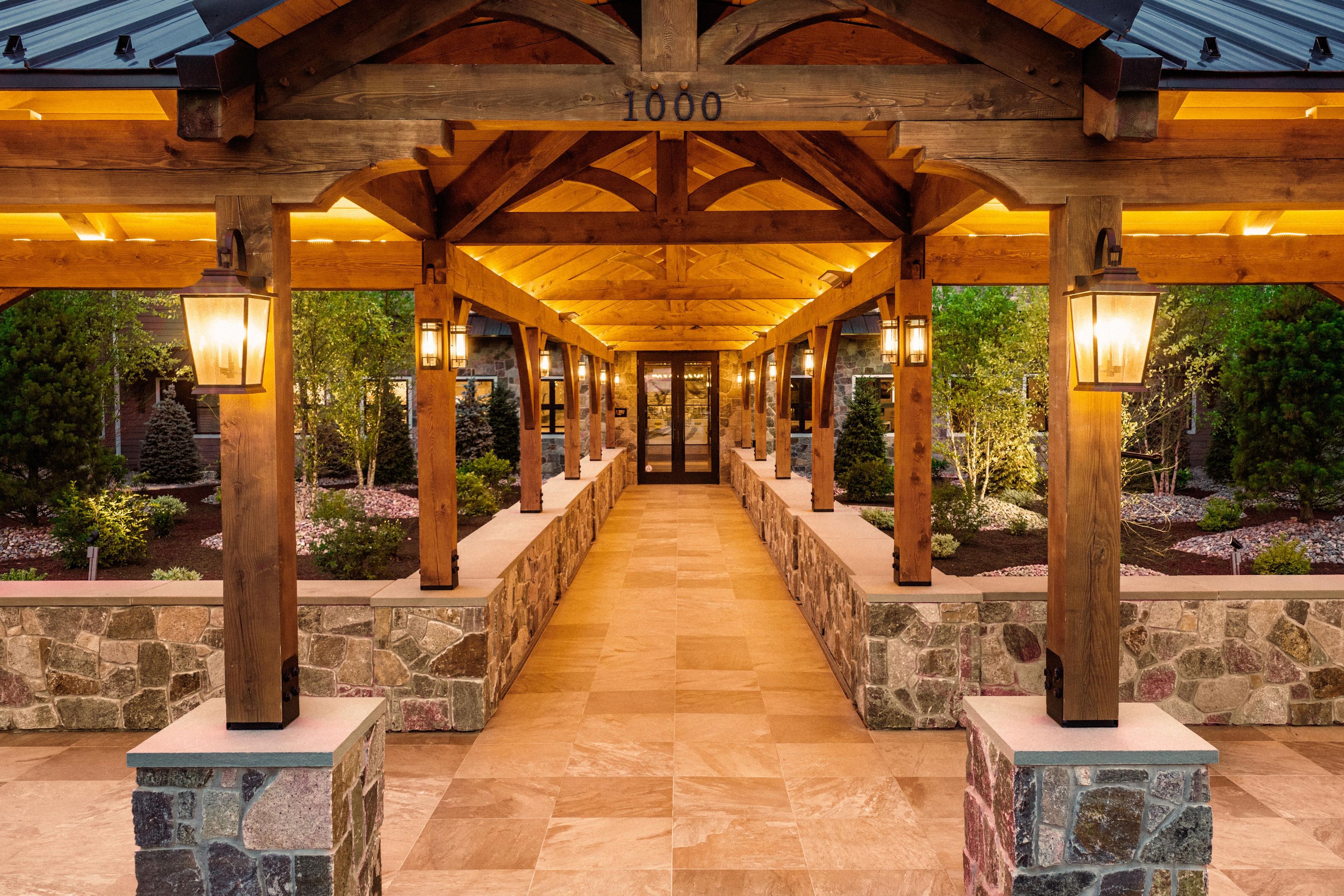 A covered walkway with stone pillars and wooden beams, leading to a building entrance.