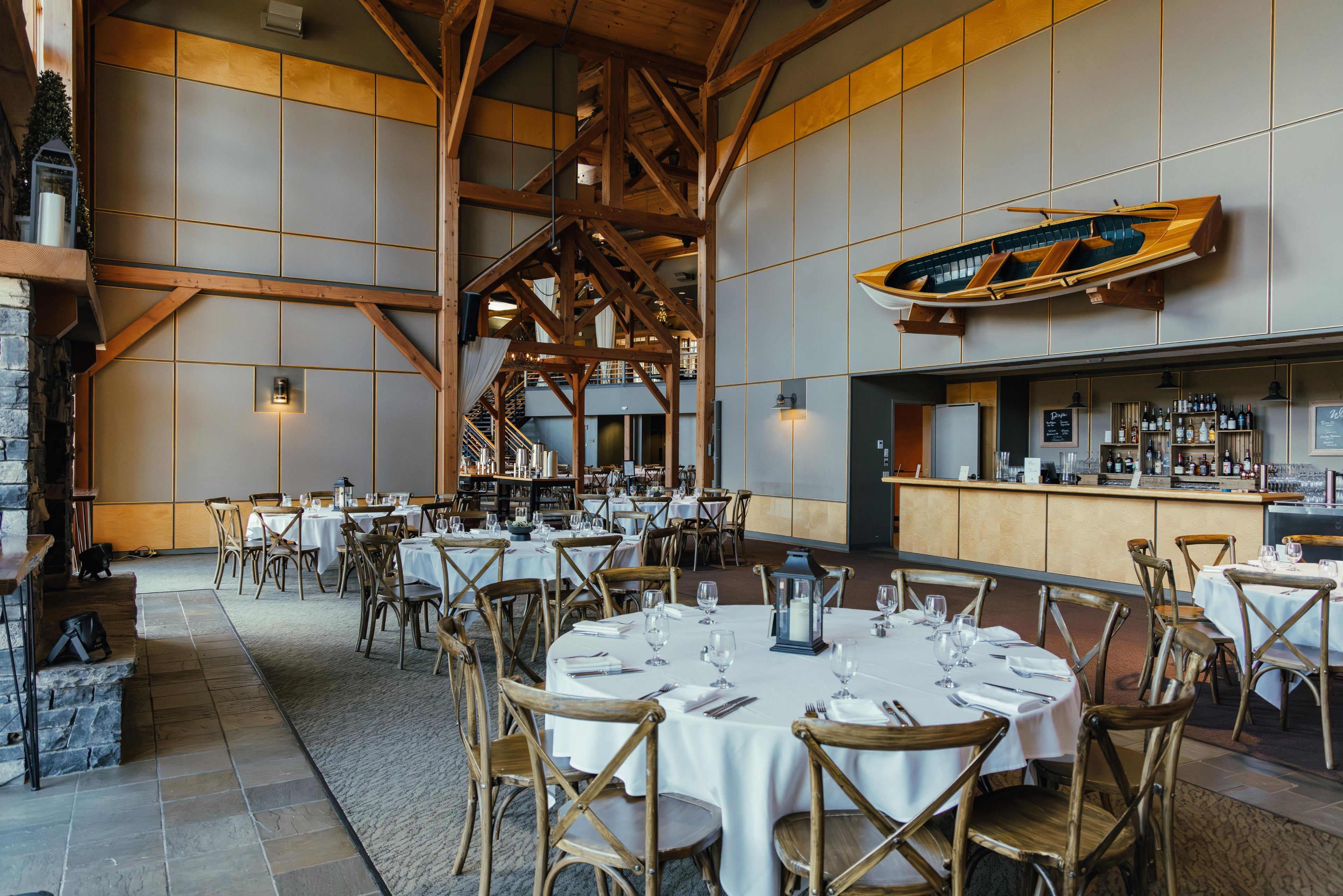 A spacious dining area with high ceilings and exposed wooden beams, featuring round tables and wooden chairs.
