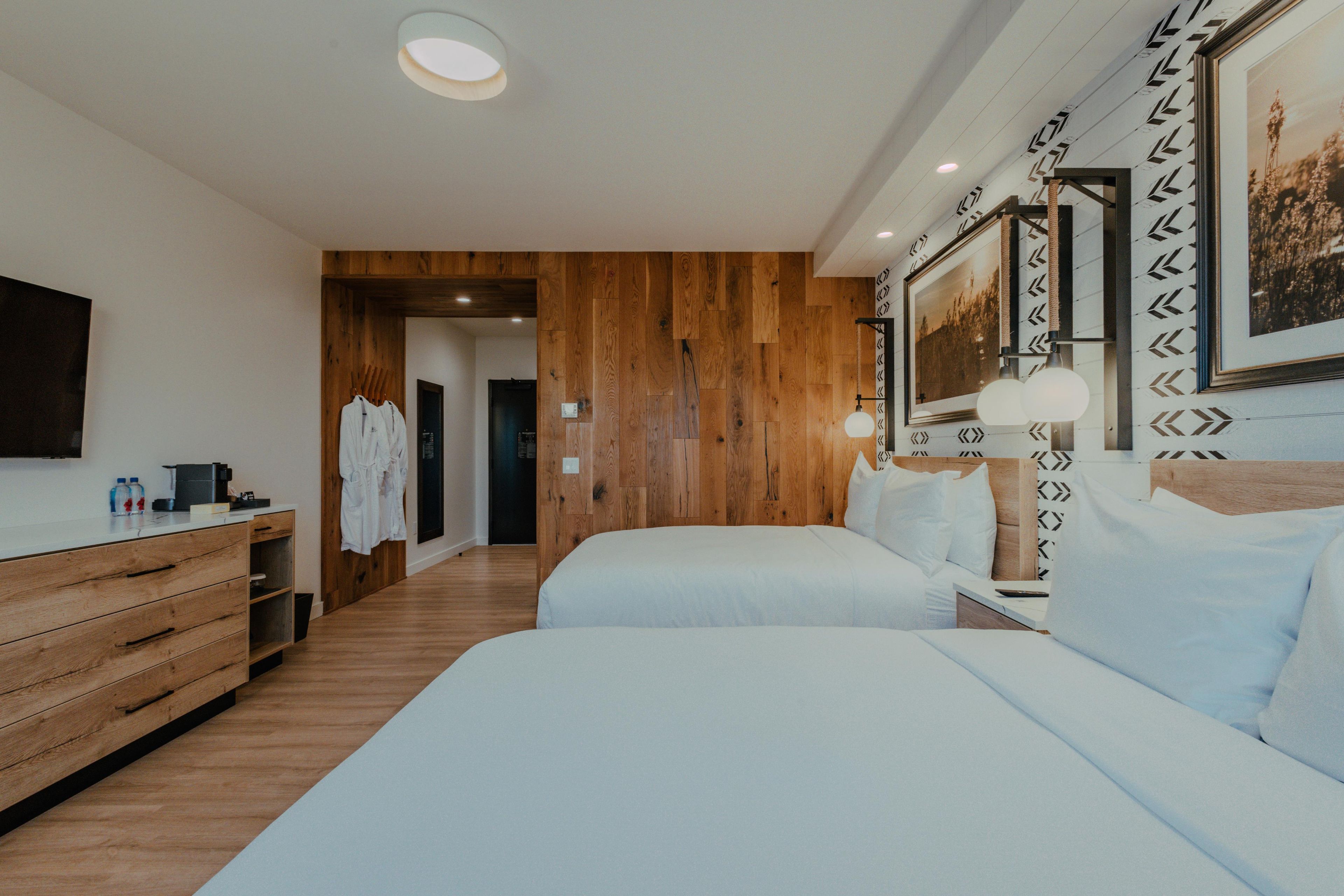 A hotel room with two beds, wooden flooring, a wooden wardrobe, a flat-screen TV, and a framed picture on the wall.