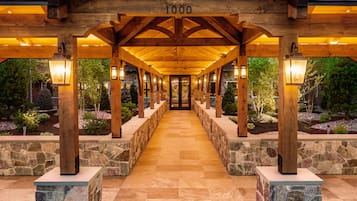 A covered walkway with stone pillars and wooden beams, leading to a building entrance.