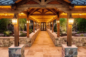 A covered walkway with stone pillars and wooden beams, leading to a building entrance.