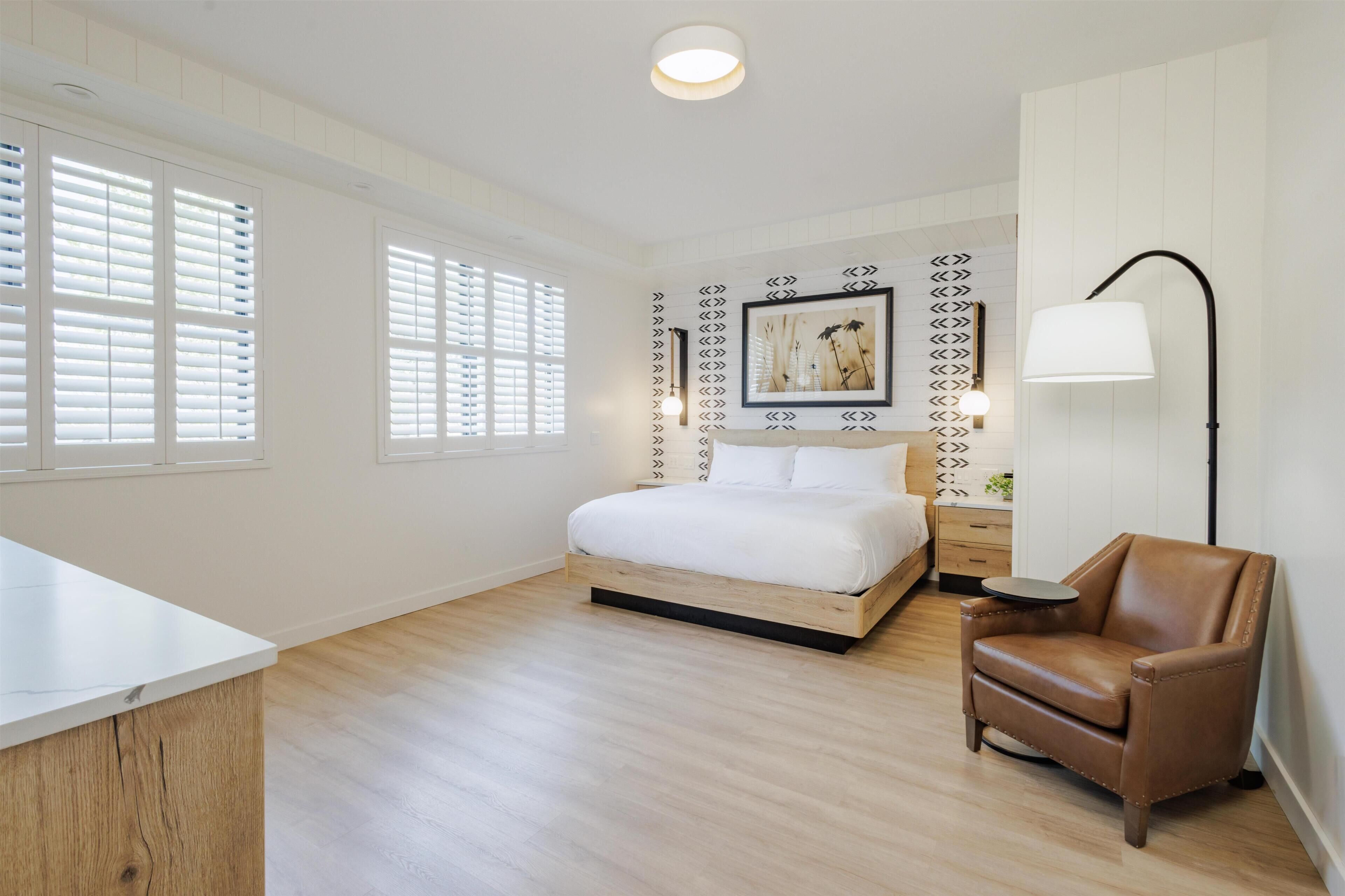 A bedroom with a bed, a chair, a bedside table, and a lamp.