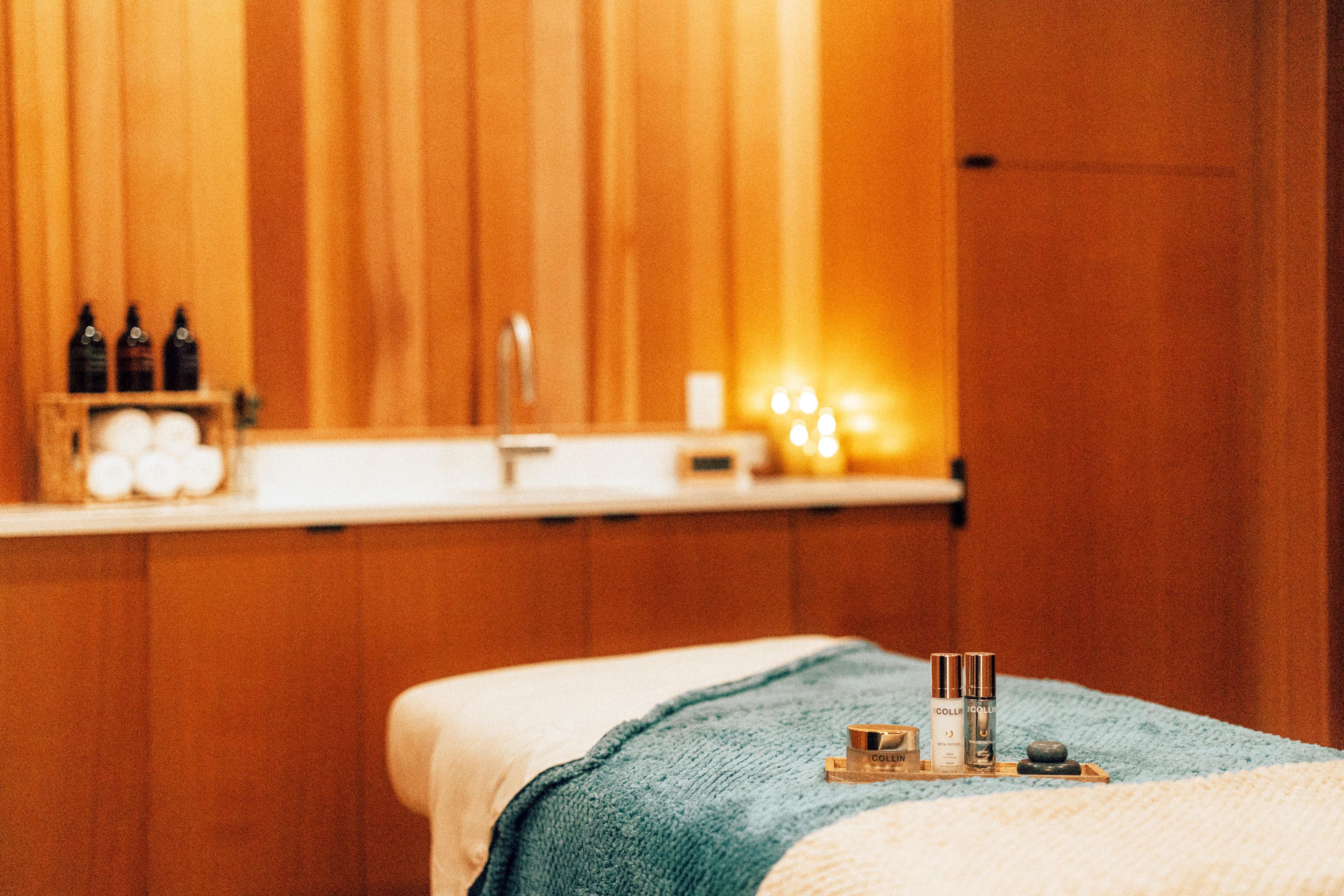 A spa room with a massage table, a wooden wall, and a shelf with bottles.