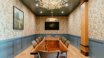 Ein Konferenzraum mit einem langen Holztisch, Stühlen, einer Chandelierleuchtre und einem Gemälde an der Wand.