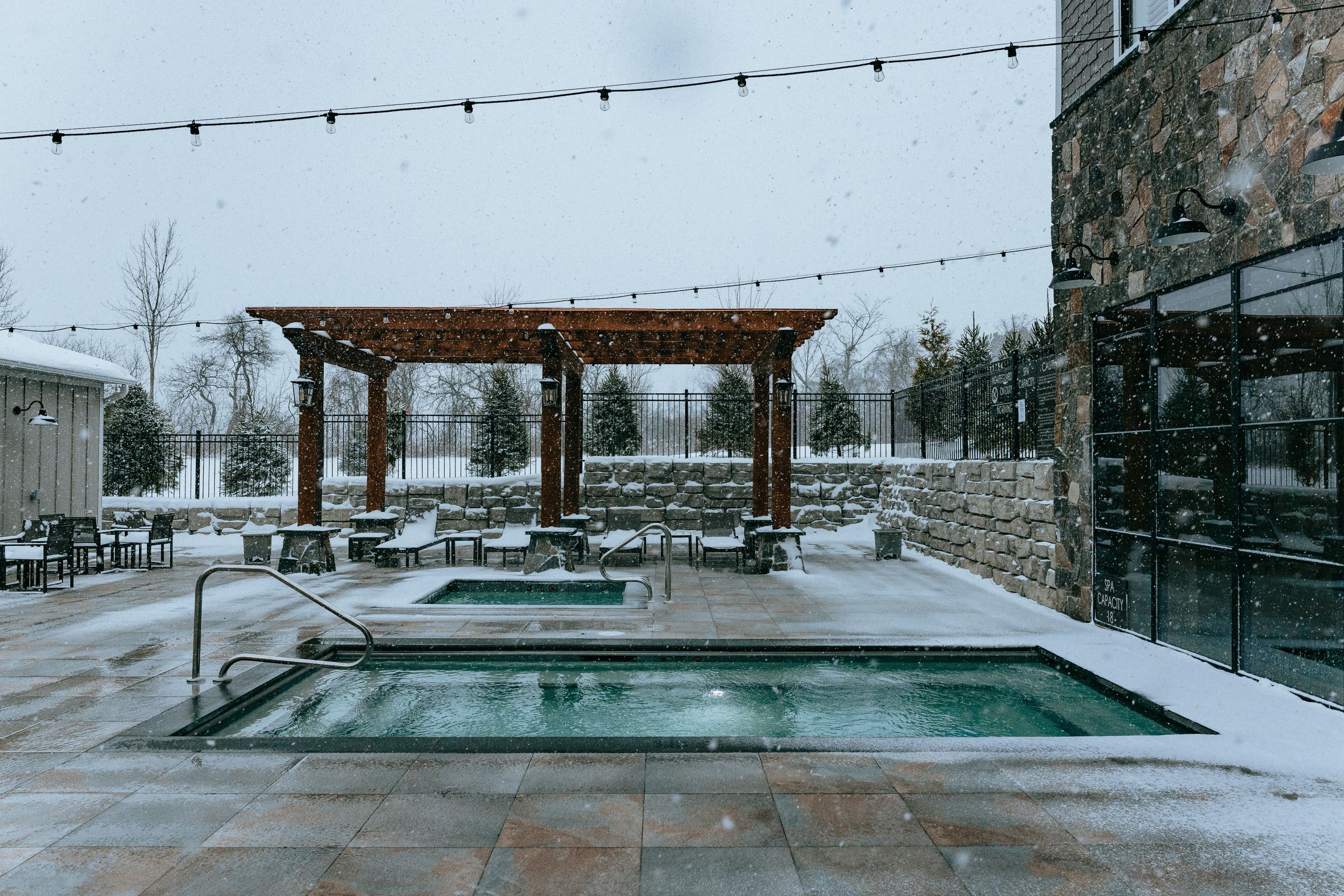 A covered outdoor area with a pool, stone walls, and string lights.