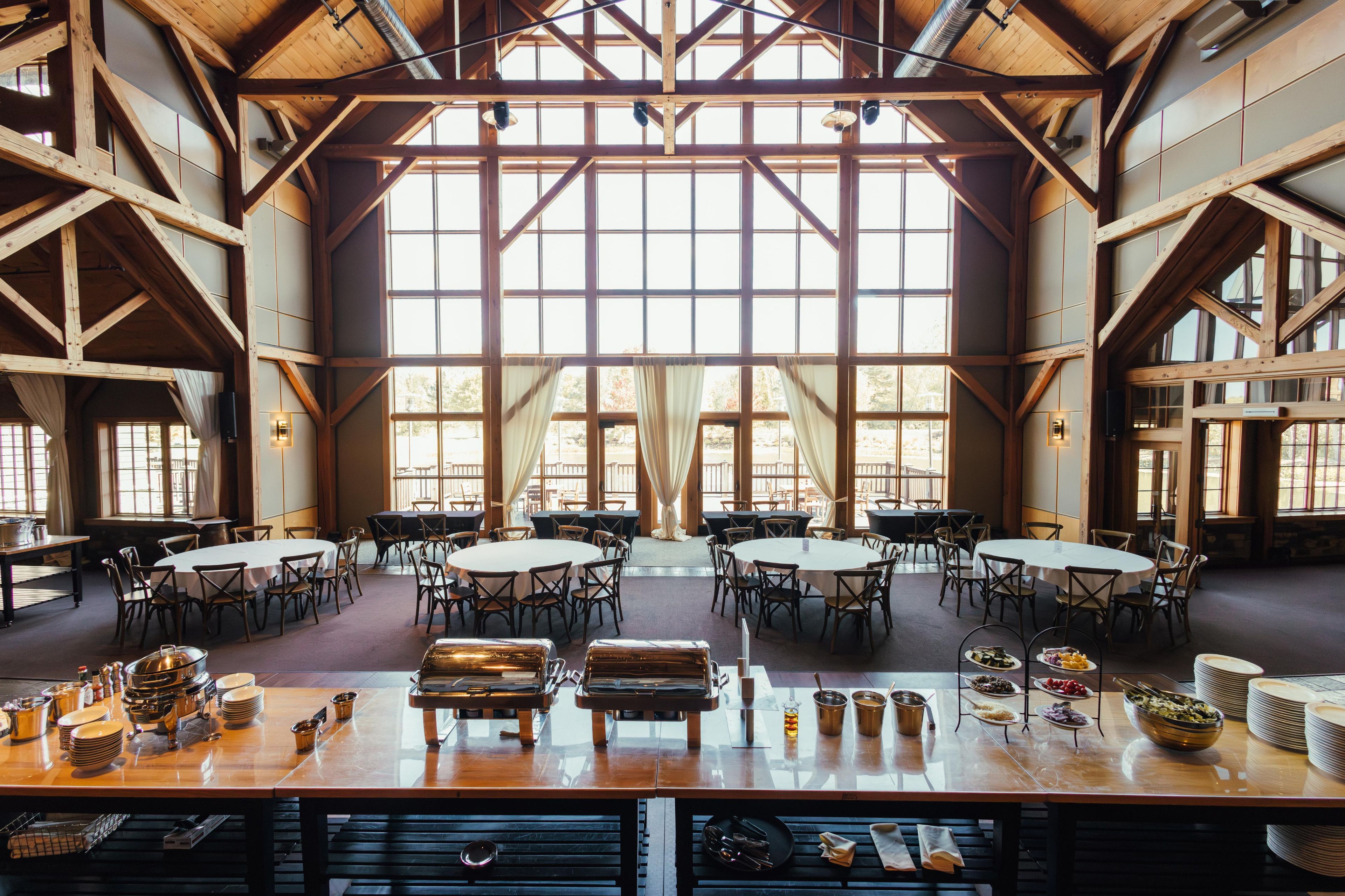 Une salle à manger spacieuse, dotée de hauts plafonds et de grandes fenêtres, et aménagée avec plusieurs tables et chaises rondes.