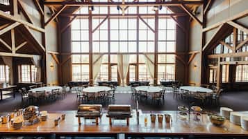Une salle à manger spacieuse, dotée de hauts plafonds et de grandes fenêtres, et aménagée avec plusieurs tables et chaises rondes.