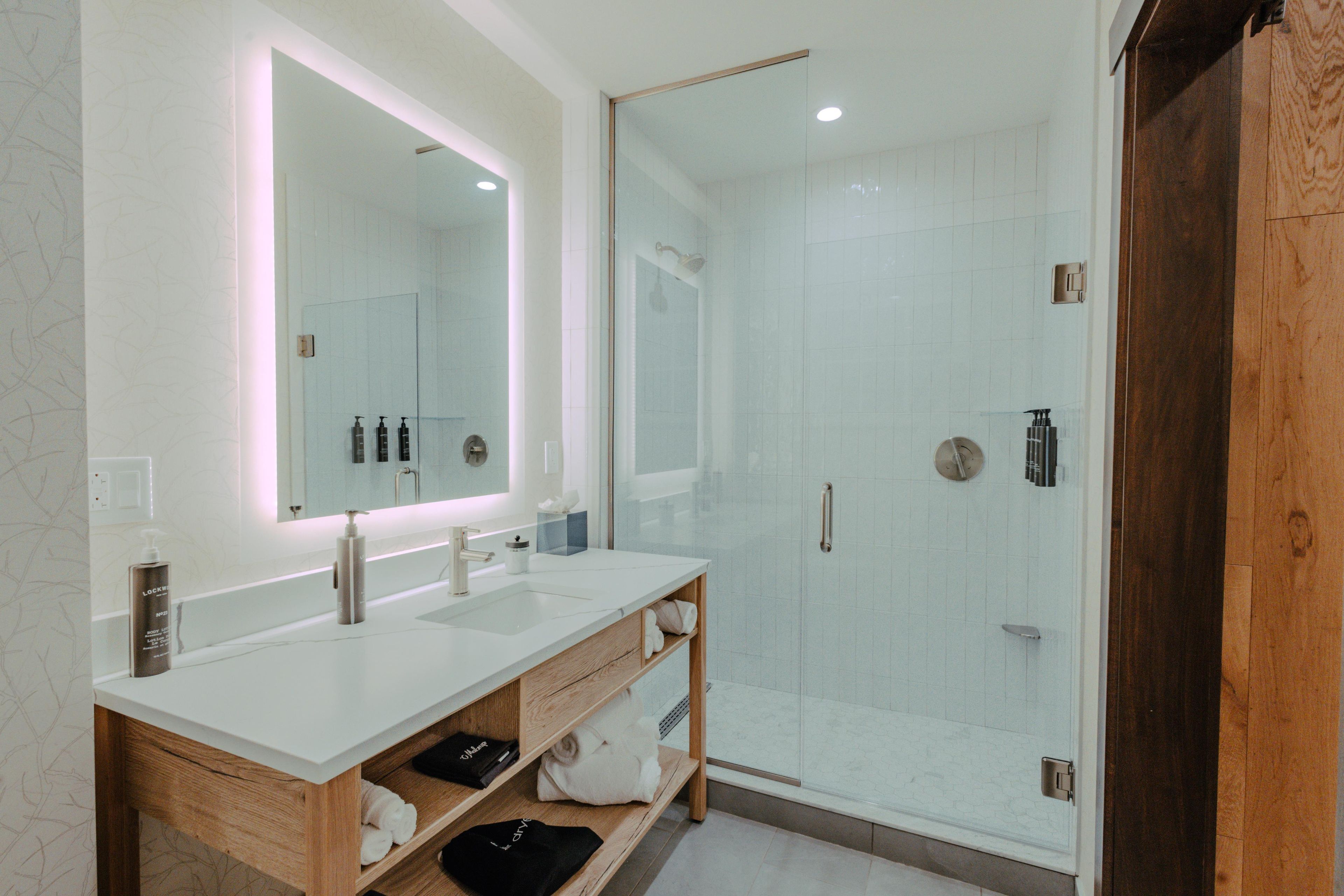 Une salle de bain moderne avec un grand miroir, deux lavabos, une douche et des meubles de rangement en bois.